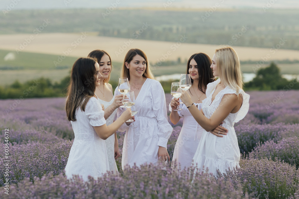 A group of women in white dresses stand in a field of lavender and smiling.