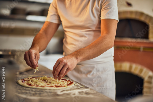 Close-up of a pizza master, making a pizza for his customers, putting cheese on top.