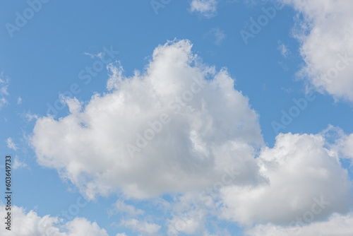 White fluffy clouds on a summer blue sky in cartoon style for background or wallpaper design. The background is white of round clouds in a blue sky. © Dmitry Presnyakov