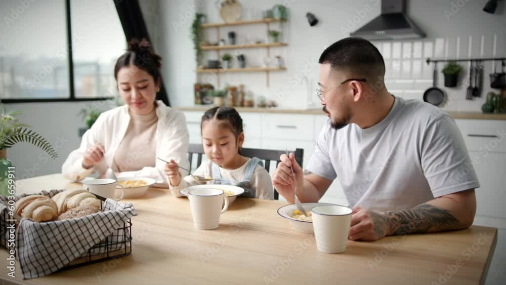 Family with one kid eating breakfast cereals. Asian mom dad and daughter eating together. Corn flakes with milk for breakfast. Family with one kid eating breakfast cereals. Asian mom dad and daughter eating together. Corn flakes with milk for breakfast.
