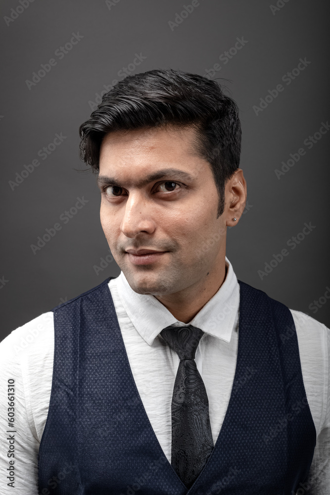 Studio shot of cheerful, young, handsome Indian male model in formal wear wearing white shirt, black tie, black coat against grey background. Male model. Fashion Portrait. Studio shot of cheerful, young, handsome Indian male model in formal wear wearing white shirt, black tie, black coat against grey background. Male model. Fashion Portrait.