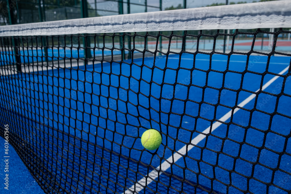 ball hitting the net of a blue paddle tennis court, racket sports concept