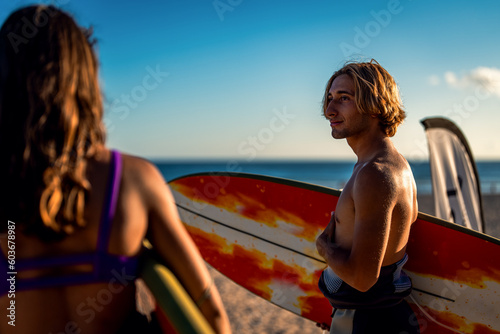 Two surfers with surfboard prepares to hit the waves at sunset.