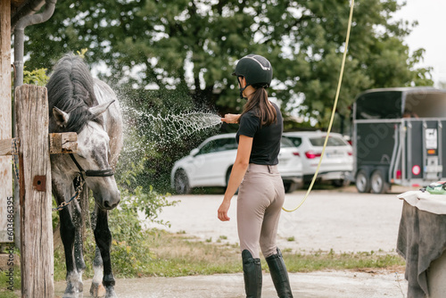 Young woman washing her horse on a farm after ride in summer