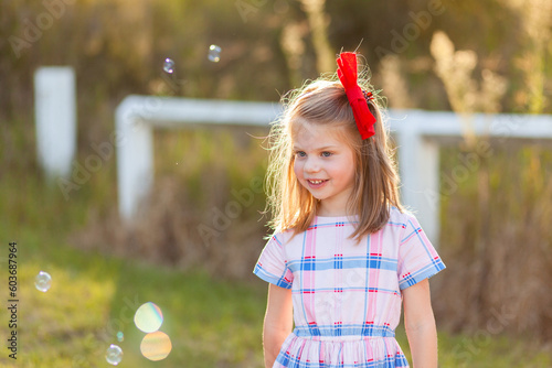 Happy girl with hidden disability standing in sunlight with bubbles at park
