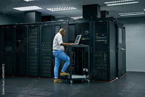 Server room, database and information technology with an engineer man at work on a network mainframe. Computer, programming and cybersecurity with a male technician working in IT support or safety photo