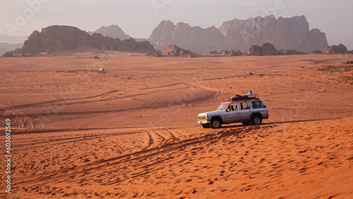 Man laying on his jeep in the Wadi Rum desert, large rock formations seen in the background.