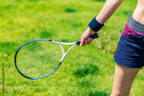 Close-up of female hands holding tennis racket on green grass background