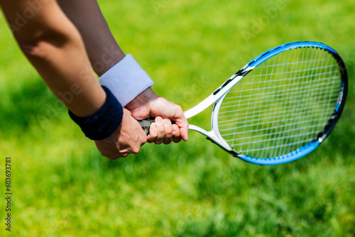 Close-up of female hands holding tennis racket on green grass background