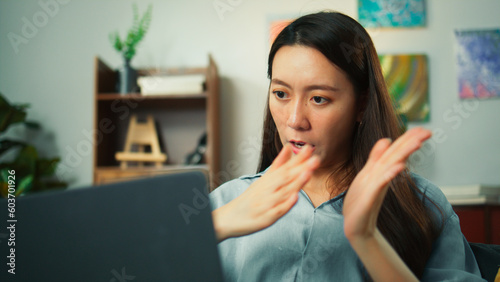 Happy attractive young Asian woman using laptop video conference call work with friends or family. Beautiful female smile looking at notebook computer screen talking sit on couch in cozy living room