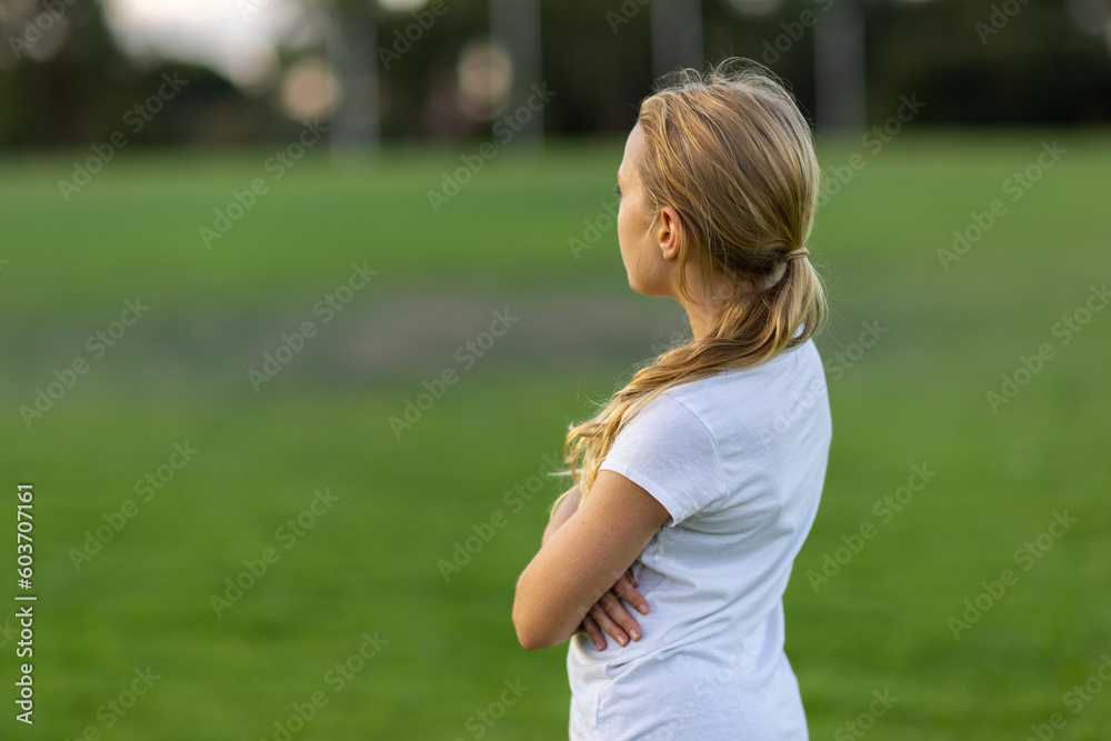 young girl from behind looking away over green playing field young girl from behind looking away over green playing field