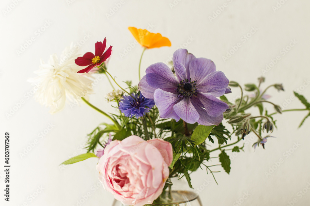 Stylish colorful flowers bouquet on rustic wall background. Beautiful summer wildflowers, anemones and roses in vase gathered from garden, floral arrangement in modern room in home