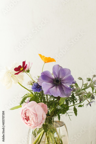 Fototapeta Naklejka Na Ścianę i Meble -  Stylish colorful flowers bouquet on rustic wall background. Beautiful summer wildflowers, anemones and roses in vase gathered from garden, floral arrangement in modern room in home