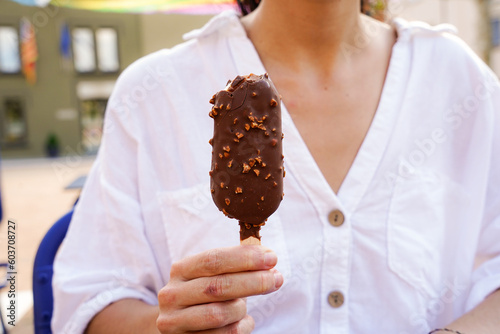 an unrecognizable woman holds a almond-shaped chocolate lolly at a town festival. ice cream in summer