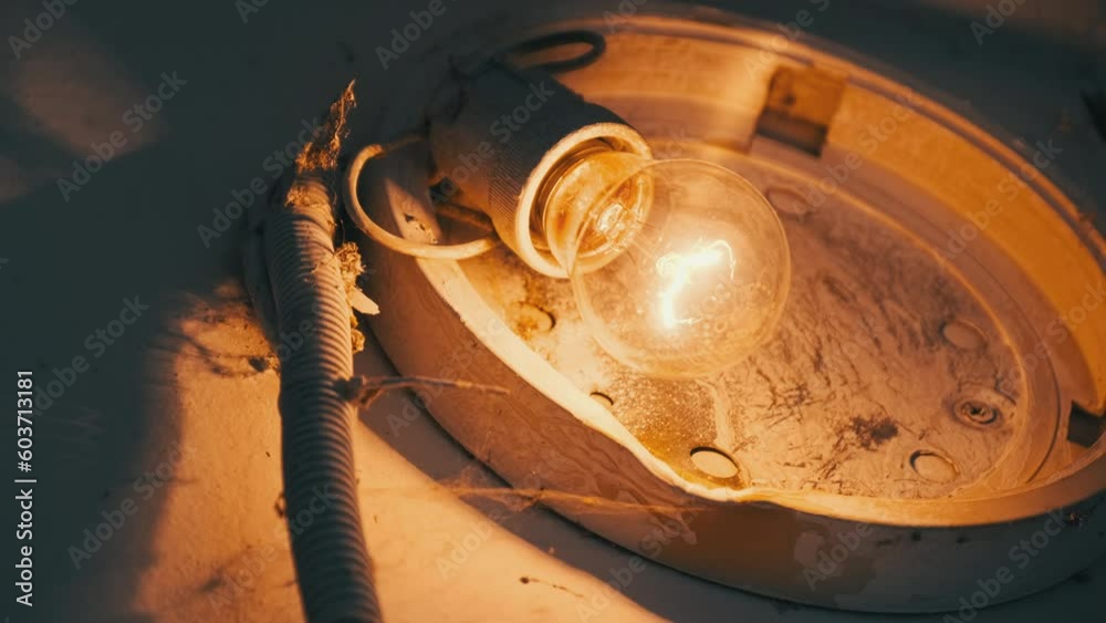 An incandescent light bulb glows in an old broken lamp on the concrete
