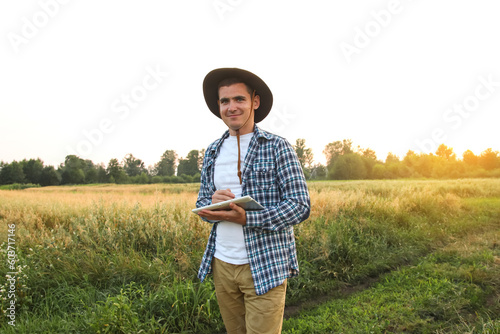 Farmer man. In the midst of a lush green wheat field, a farmer stands holding a tablet in his hands, embodying the concept of a smart farm. Sunset