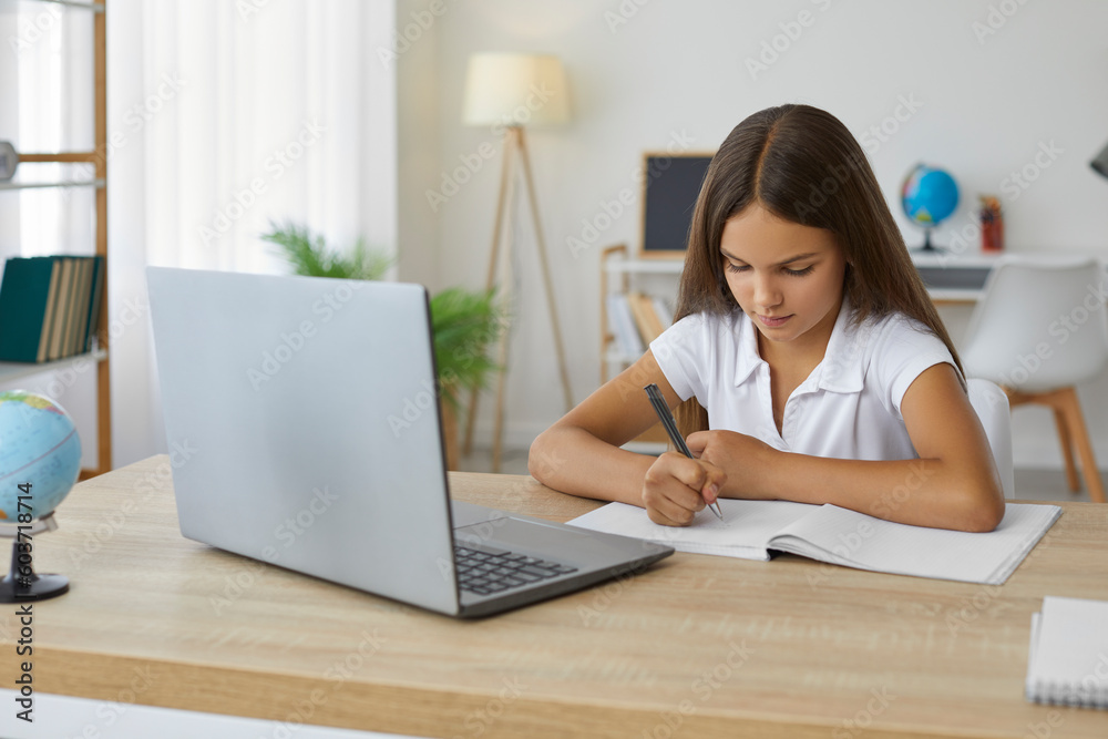 School child doing homework. Little kid doing school assignment at home. Pretty girl sitting at desk in her beautiful room, writing in notebook, and using modern laptop computer