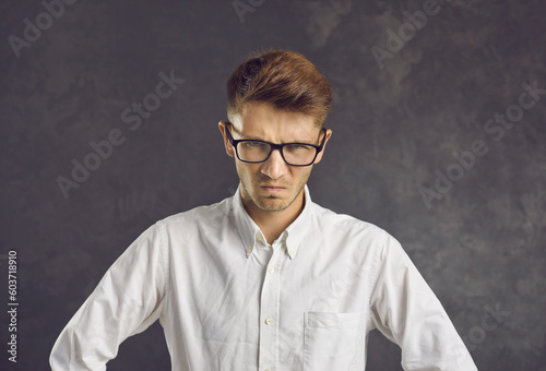 Portrait of furious young Caucasian man in glasses on black studio background feel mad distressed with problems. Unhappy angry male look at camera have anger rage. Negative emotion control concept.