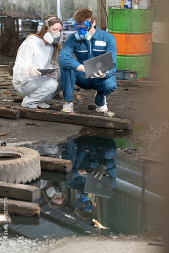 emergency pollution factory concept. engineers wearing mechanic jumpsuits and ppe and gas masks inspect oil on the factory floor.