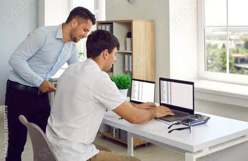 Financial accountant or businessman and his male assistant work together with data lists. Two men in office are working with two laptops with open spreadsheets. Business, finance and teamwork concept. photo