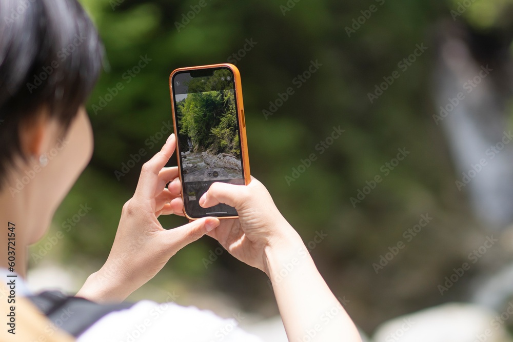 日本の山をトレッキングしている日本人女性/
携帯で景色の写真を撮っている