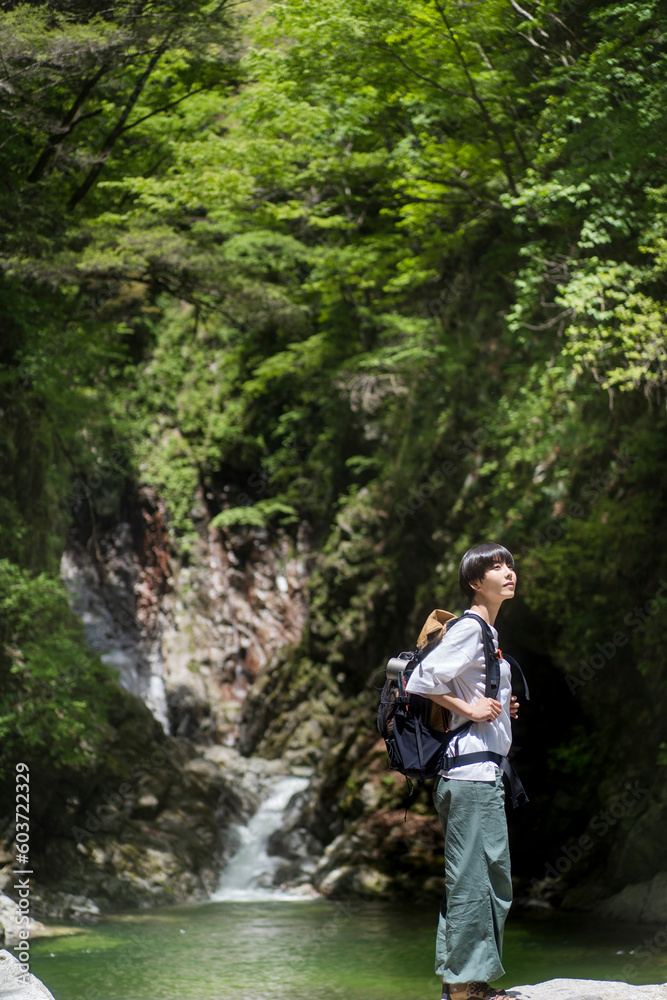 日本に山をトレッキングする日本人女性/
滝壺で景色を眺めながら休憩をしている