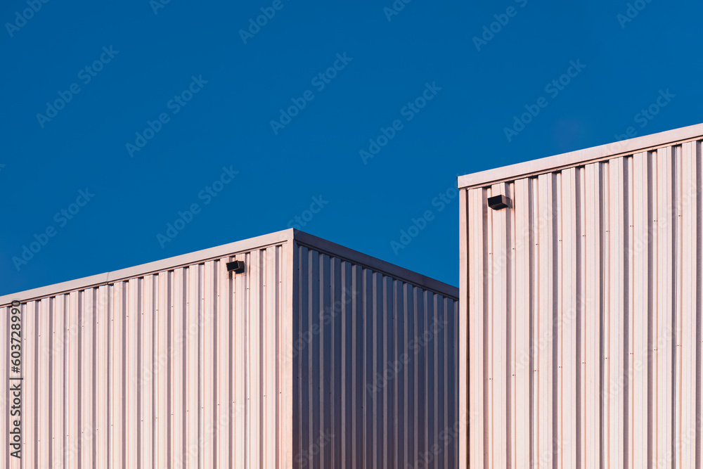 Two Aluminium Corrugated Warehouse Building against blue clear sky Background with light reflection on surface, perspective side view Two Aluminium Corrugated Warehouse Building against blue clear sky Background with light reflection on surface, perspective side view