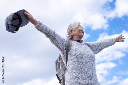 Happy active senior woman in outdoors hiking day holding backpack looking at the sky with open arms enjoying freedom photo