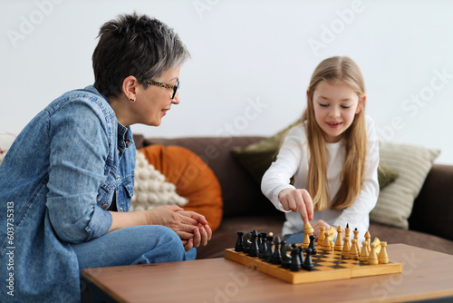 Little girl child and adult woman playing chess in home interior.