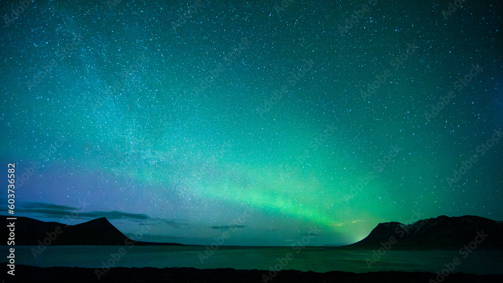 Green sky of Northern Lights above sea and hills in Iceland