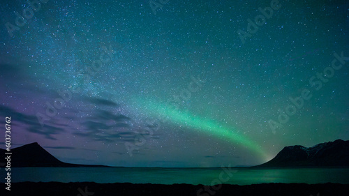 Swoosh of Northern Lights above the sea and hills in Iceland