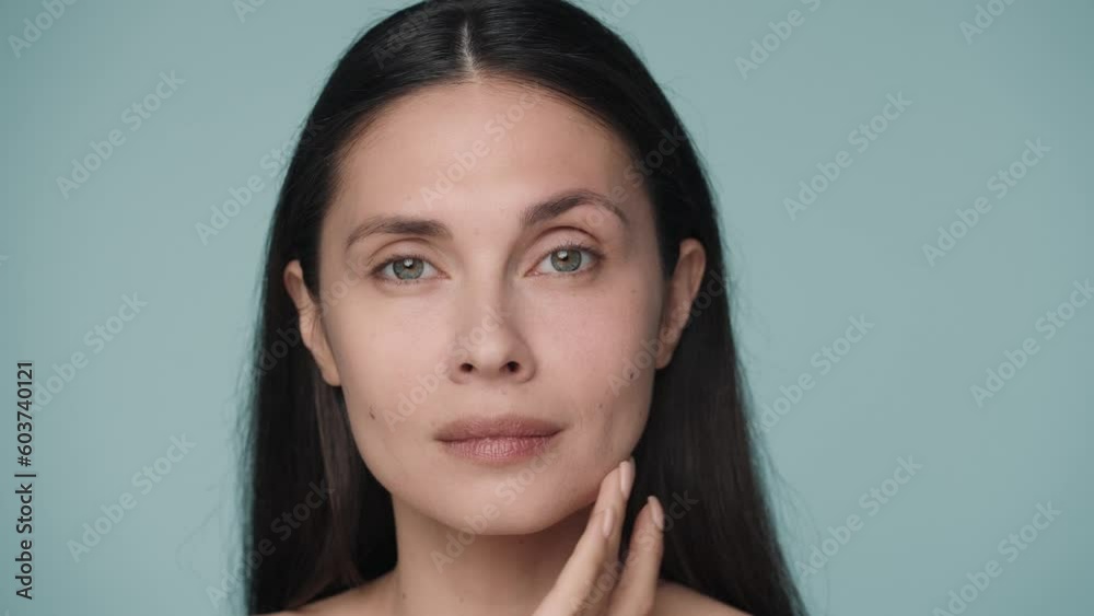 A seminude brunette woman massages the skin around the eyes. A young woman struggles with mimic wrinkles by gently massaging the skin under her eyes. Portrait of a woman on a blue background close up. A seminude brunette woman massages the skin around the eyes. A young woman struggles with mimic wrinkles by gently massaging the skin under her eyes. Portrait of a woman on a blue background close up.