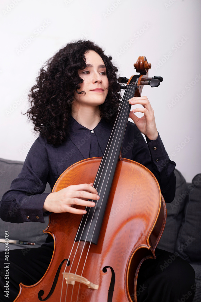 Female musician playing cello while sitting on sofa Female musician playing cello while sitting on sofa