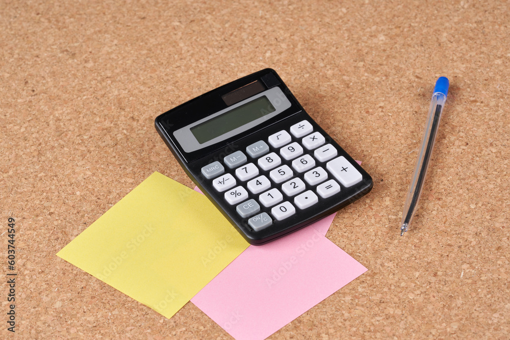Calculator and pen on a cork plate. Calculator and pen on a cork plate.