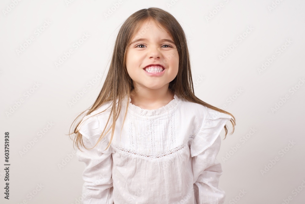 Cute charming little girl wearing white shirt over white background clenching teeth feeling excited or angry. Cute charming little girl wearing white shirt over white background clenching teeth feeling excited or angry.