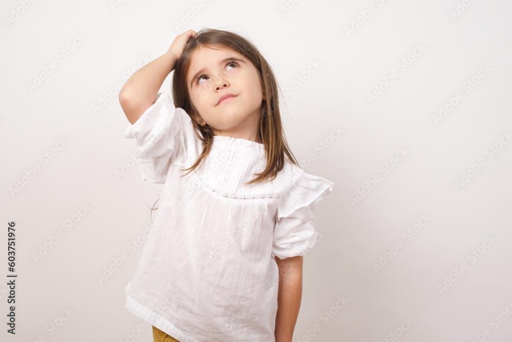 Cute charming little girl wearing white shirt over white background holding hand on her head having a dreamy thoughtful look. Cute charming little girl wearing white shirt over white background holding hand on her head having a dreamy thoughtful look.