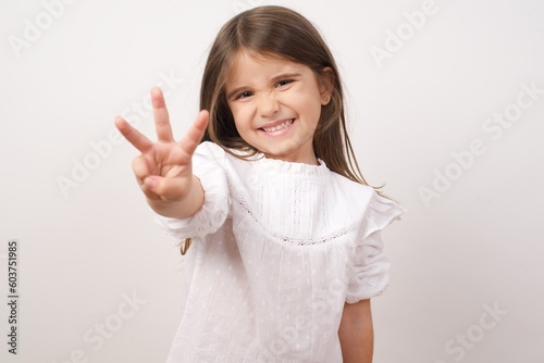 Cute charming little girl wearing white shirt over white background pointing up with fingers number three, third, 