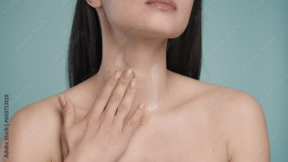 A woman applies cream to her neck and upper body. With slow massage movements, a woman rubs the cream into the skin close-up on a blue background. The concept of skin and body care. Natural beauty. A woman applies cream to her neck and upper body. With slow massage movements, a woman rubs the cream into the skin close-up on a blue background. The concept of skin and body care. Natural beauty.