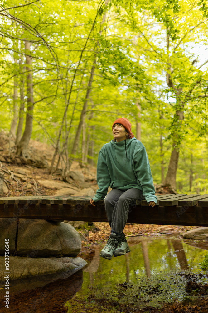 woman in the forest sitting on a bridge with orange cap hat, on a trip looking for new to discover, looking up woman in the forest sitting on a bridge with orange cap hat, on a trip looking for new to discover, looking up