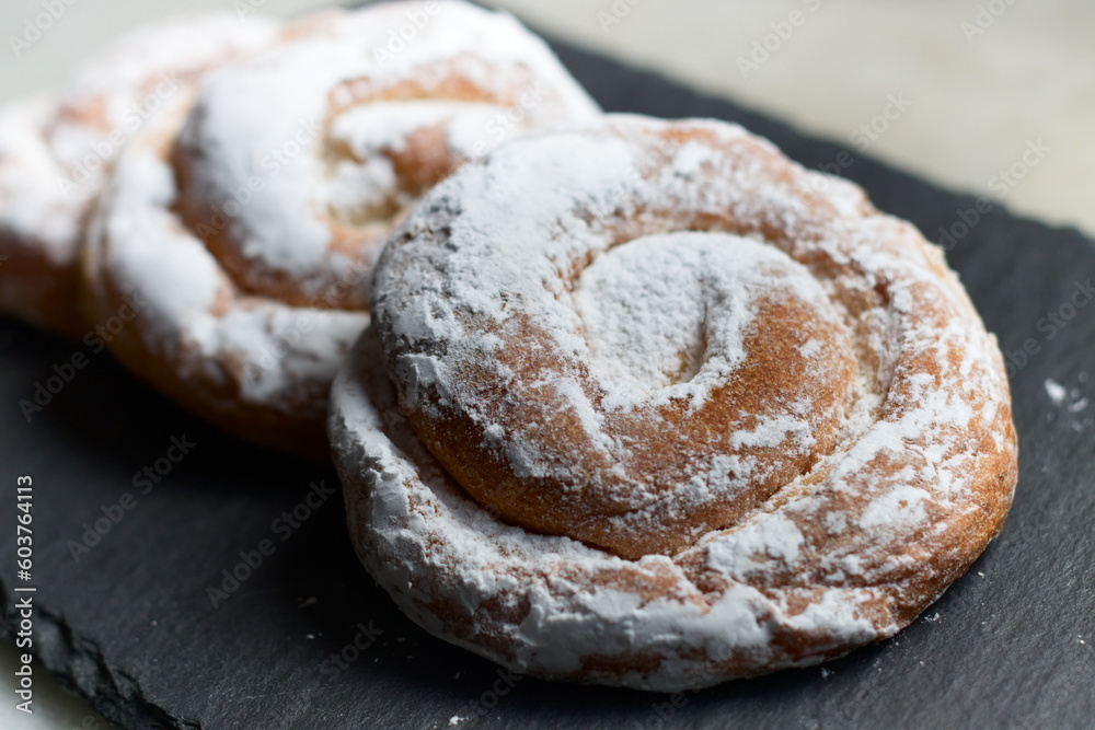 closeup of some ensaimadas with icing sugar on a slate table closeup of some ensaimadas with icing sugar on a slate table