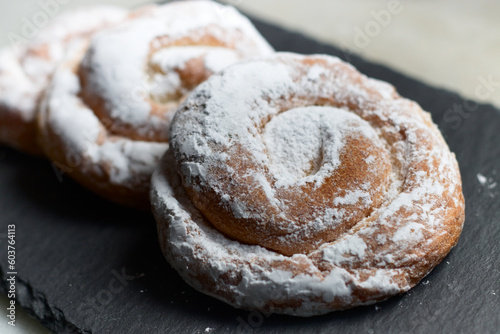 Fototapeta Naklejka Na Ścianę i Meble -  closeup of some ensaimadas with icing sugar on a slate table