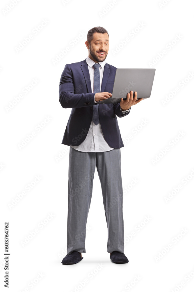 Full length portrait of a businessman in a suit and bottom pajamas standing and using a laptop computer Full length portrait of a businessman in a suit and bottom pajamas standing and using a laptop computer