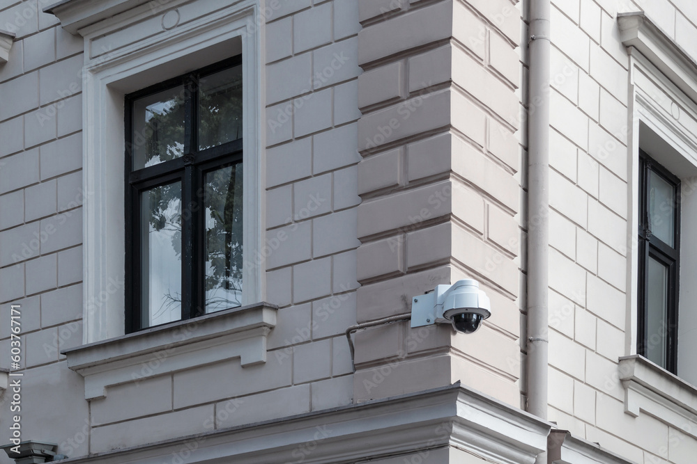 A modern security video surveillance camera on the wall of a masonry building. CCTV camera attached to the wall of the house A modern security video surveillance camera on the wall of a masonry building. CCTV camera attached to the wall of the house