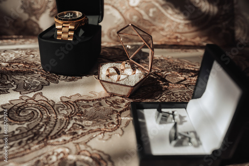 Accessories for the groom's wedding. A gold watch, gold rings, silver cufflinks on a golden tablecloth. Men's fashion and style photo