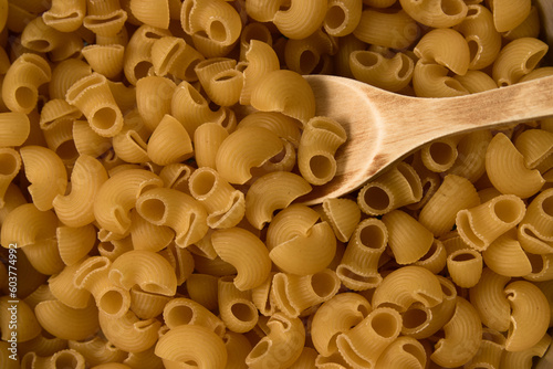 Flat lay of a bowl full of raw pasta shaped like twisted tubes called sharks with a wooden spoon