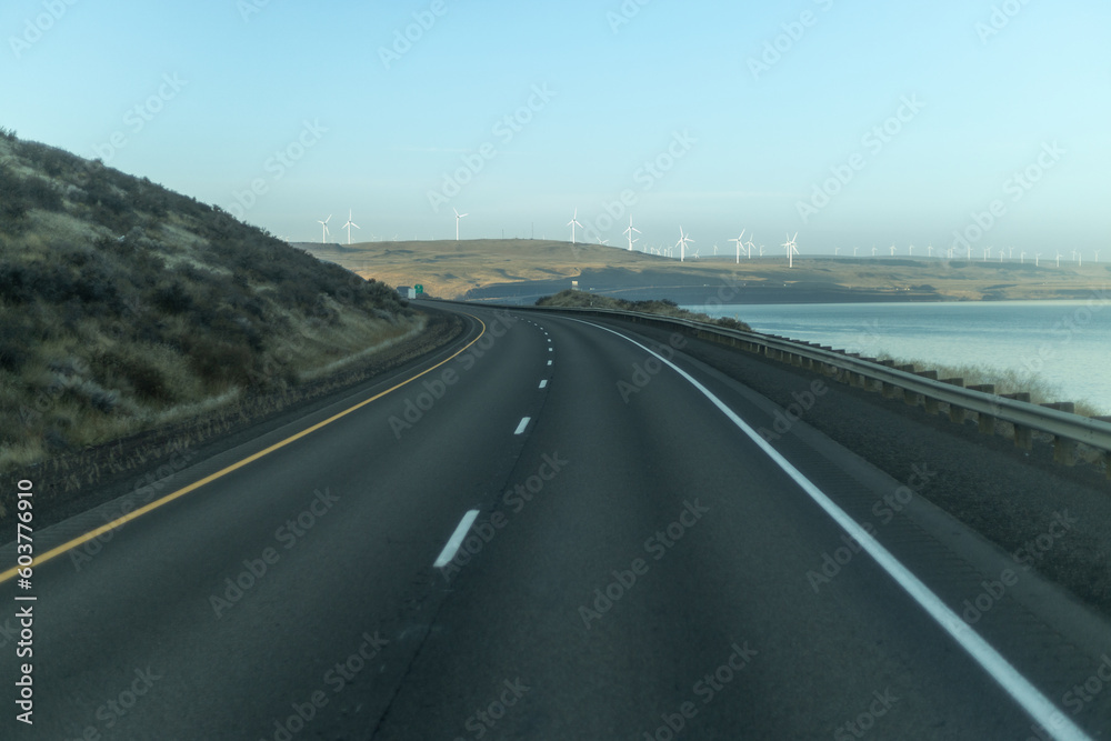 Highway with a view of the ocean and a wind farm in the distance.