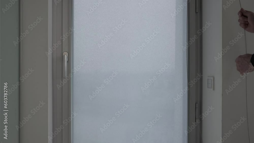 opening a gray fabric roller shade at a window in a skyscraper office building opening a gray fabric roller shade at a window in a skyscraper office building