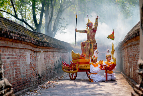 Khon or traditional Thai classic masked from the Ramakien as character of red giant stand and dance on traditional chariot also hold weapon stay in front of ancient building with mist or fog. photo