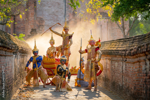 Small group of Khon or traditional Thai classic masked from the Ramakien characters stand together with action of traditional dance with Thai ancient building in background.