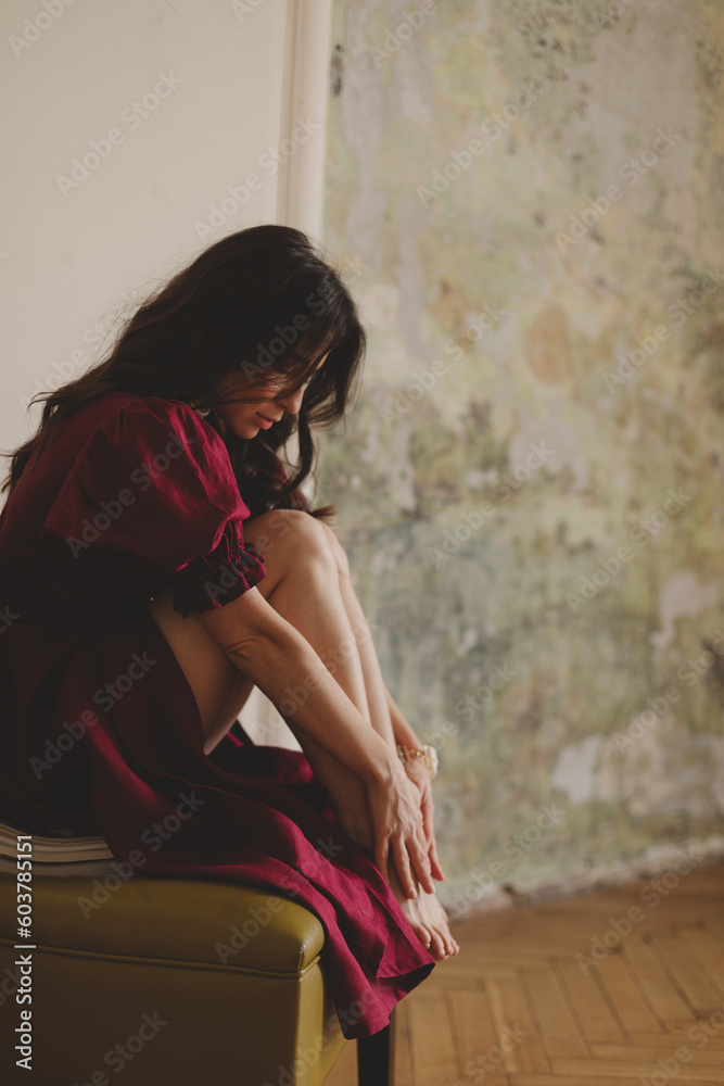 Naklejka premium Girl in the cherry dress sitting on green chair. Women's health, sexuality. Portrait of a beautiful young woman in cherry dress with belt and puff sleeves. Sexy brunette woman look sensual.